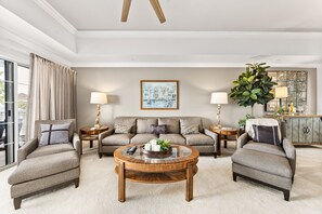 Ein geräumiges Wohnzimmer mit einer großen Sofagarnitur, zwei Sesseln, einem Couchtisch und einer üppigen Pflanze.