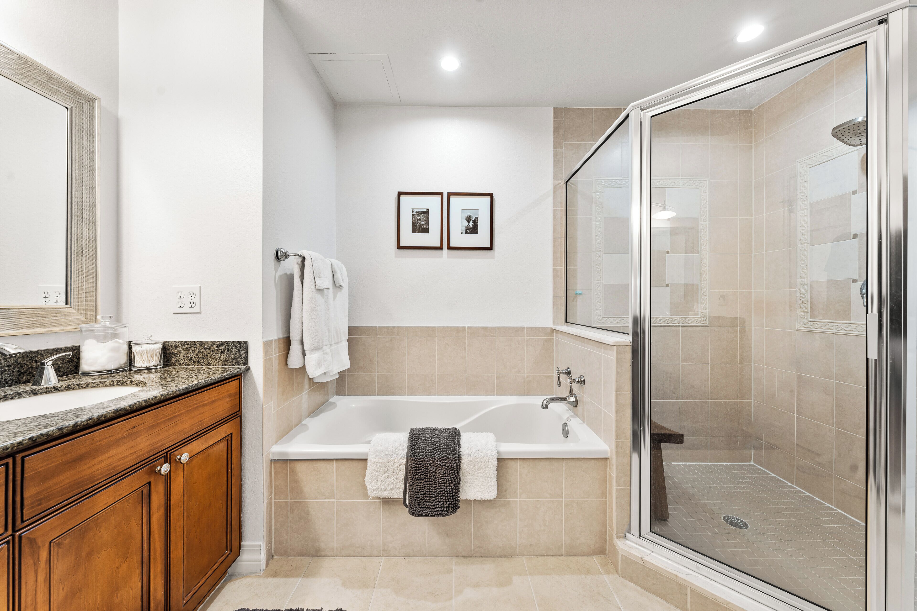 A modern bathroom with a large bathtub, a glass-enclosed shower, wooden cabinets, and two framed pictures on the wall.
