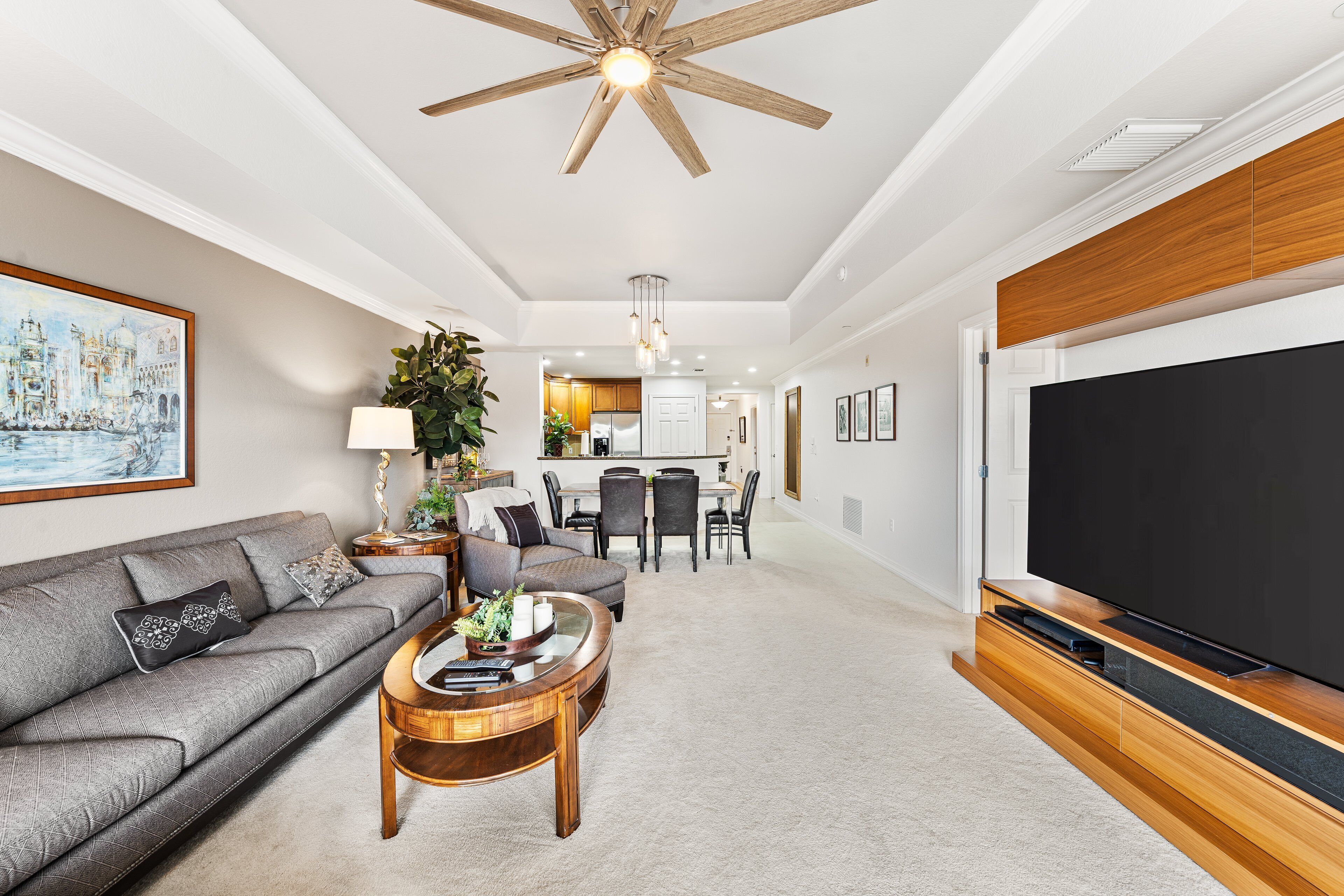 A modern living room with a sofa, coffee table, TV, and a dining area in the background.