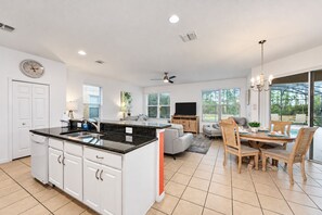 A modern kitchen with a central island, a dining area with wooden chairs, a flat-screen TV, and a ceiling fan. - Home with Screened Private Pool and Preserve Views (Davenport)