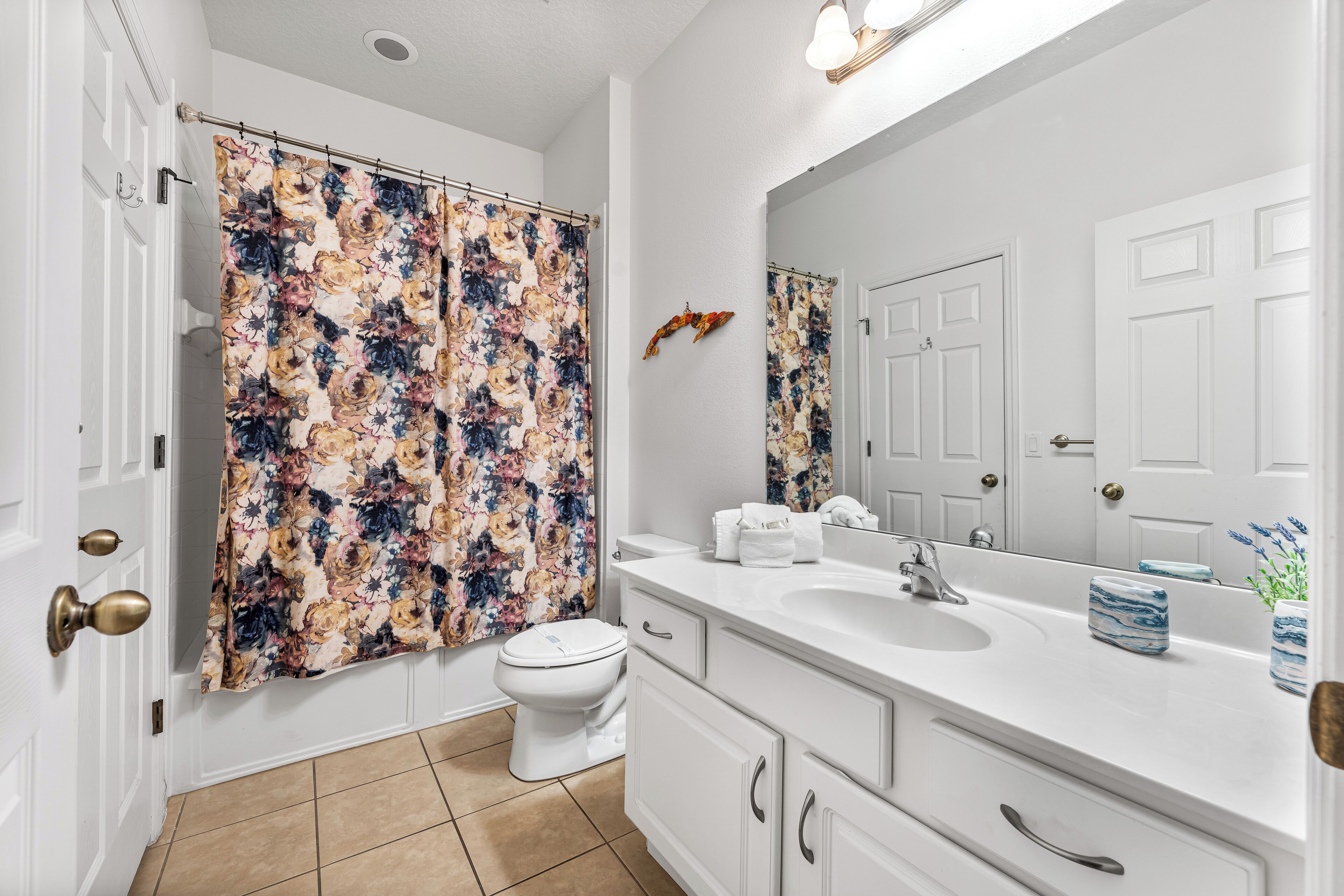 Ein Badezimmer mit Blumen-Duschvorhang, Toilette, Waschbecken mit Spiegel und Schrank.