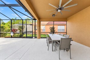 A spacious patio with a dining table and chairs, a ceiling fan, and a view of a house with a red roof. - Home with Screened Private Pool and Preserve Views (Davenport)