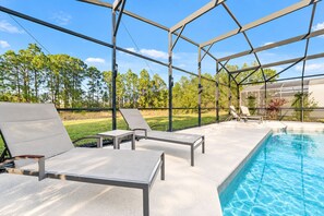 A poolside area with lounge chairs, a table, and a clear view of a swimming pool. - Home with Screened Private Pool and Preserve Views (Davenport)