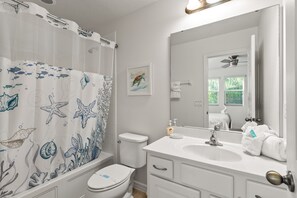 Een badkamer met douchegordijn met afbeeldingen van zeedieren, toilet, wastafel met spiegel en een handdoekhouder.