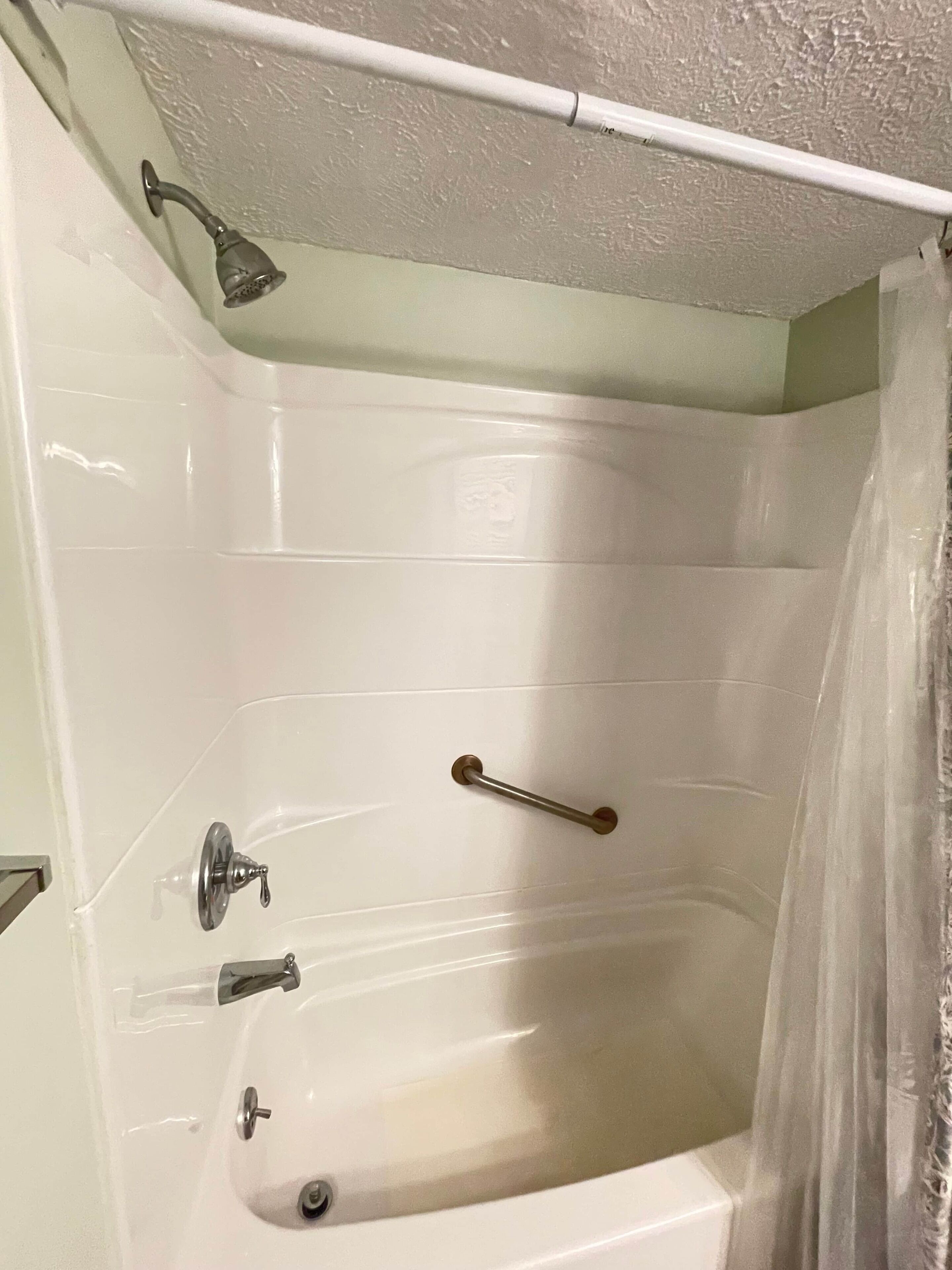 Een badkamer met een bad, douche en een handgreep.