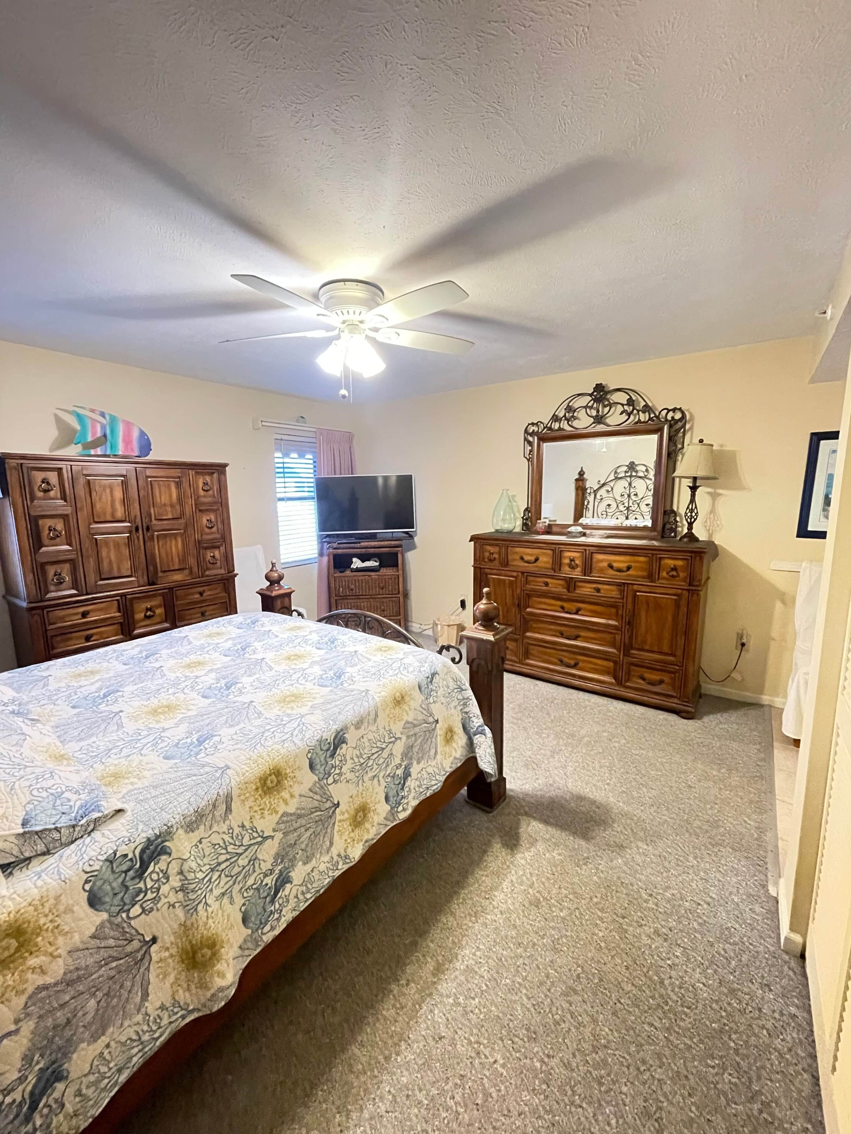 A bedroom with a bed, a ceiling fan, a dresser, a television, and a mirror.