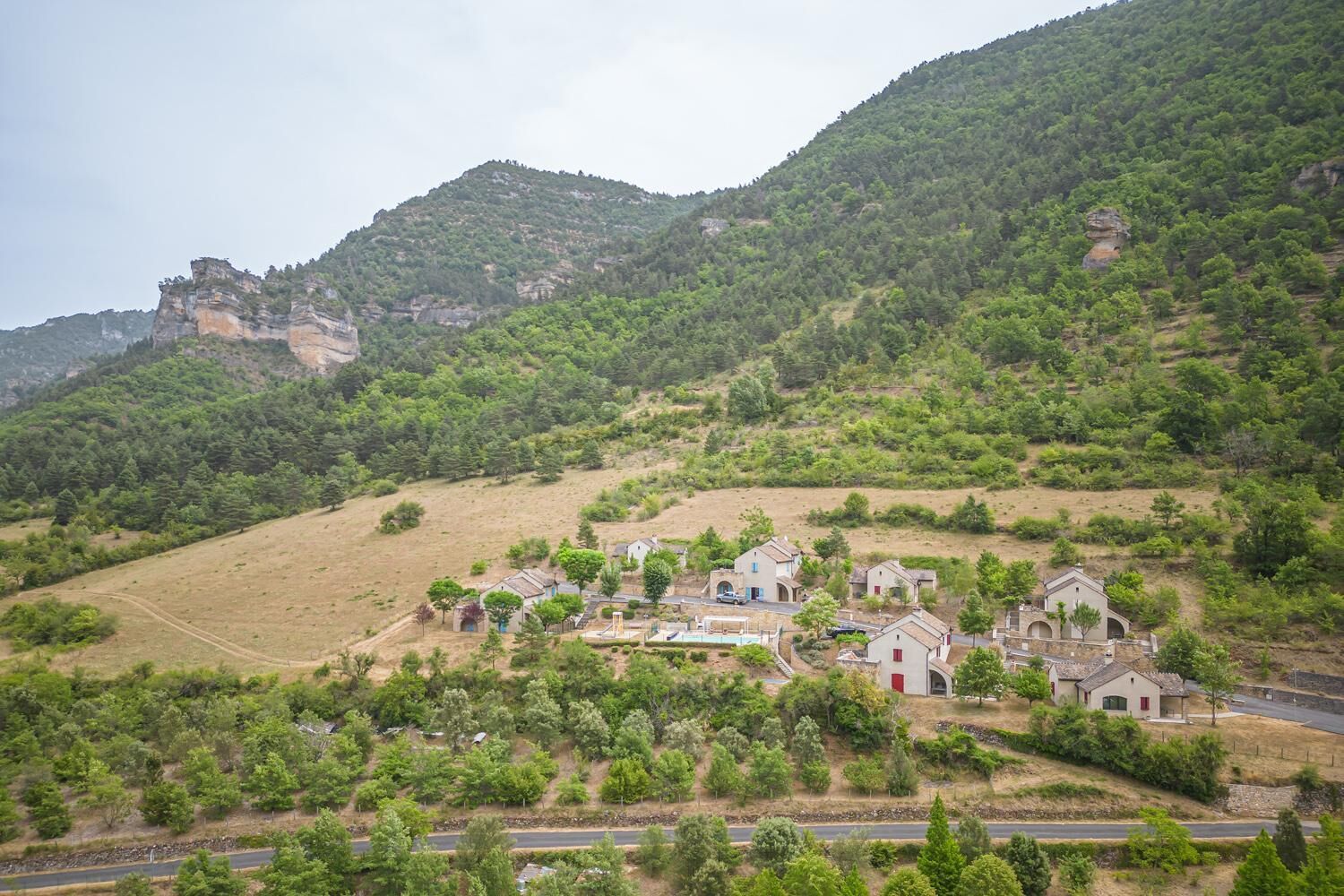 A rural village with houses on a hillside, surrounded by greenery and a prominent rocky hill in the background.