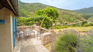 Patio esterno con tavolo e sedie, un muro in pietra e vista su una collina con case.