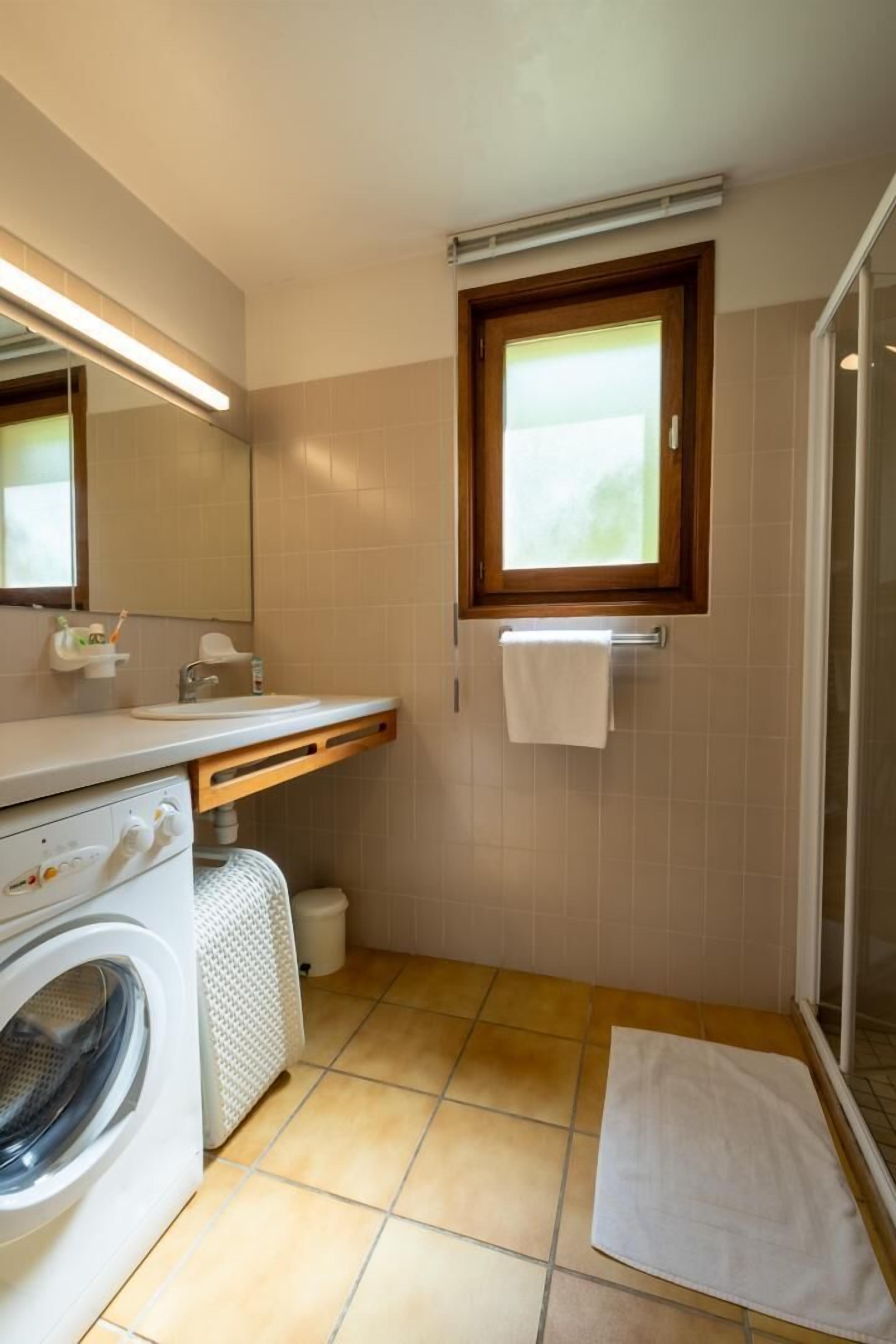 Un baño pequeño con lavadora, lavamanos, toallero y ventana.
