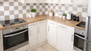 Eine moderne Küche mit weißen Schränken, einer Holz Arbeitsplatte und Edelstahlgeräten, darunter ein Backofen und ein Kühlschrank.