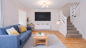 Ein Wohnzimmer mit blauem Sofa, Couchtisch, Fernseher, Heizkörper und Treppe.