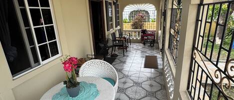 A covered balcony with a tiled floor, white wicker furniture, and a potted plant.