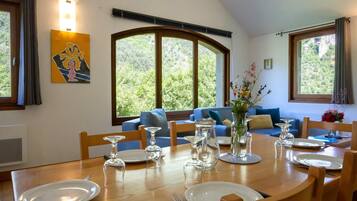 Comedor con una mesa de madera dispuesta para cuatro personas, rodeado de sofás azules y un ventanal con vistas a zonas verdes.