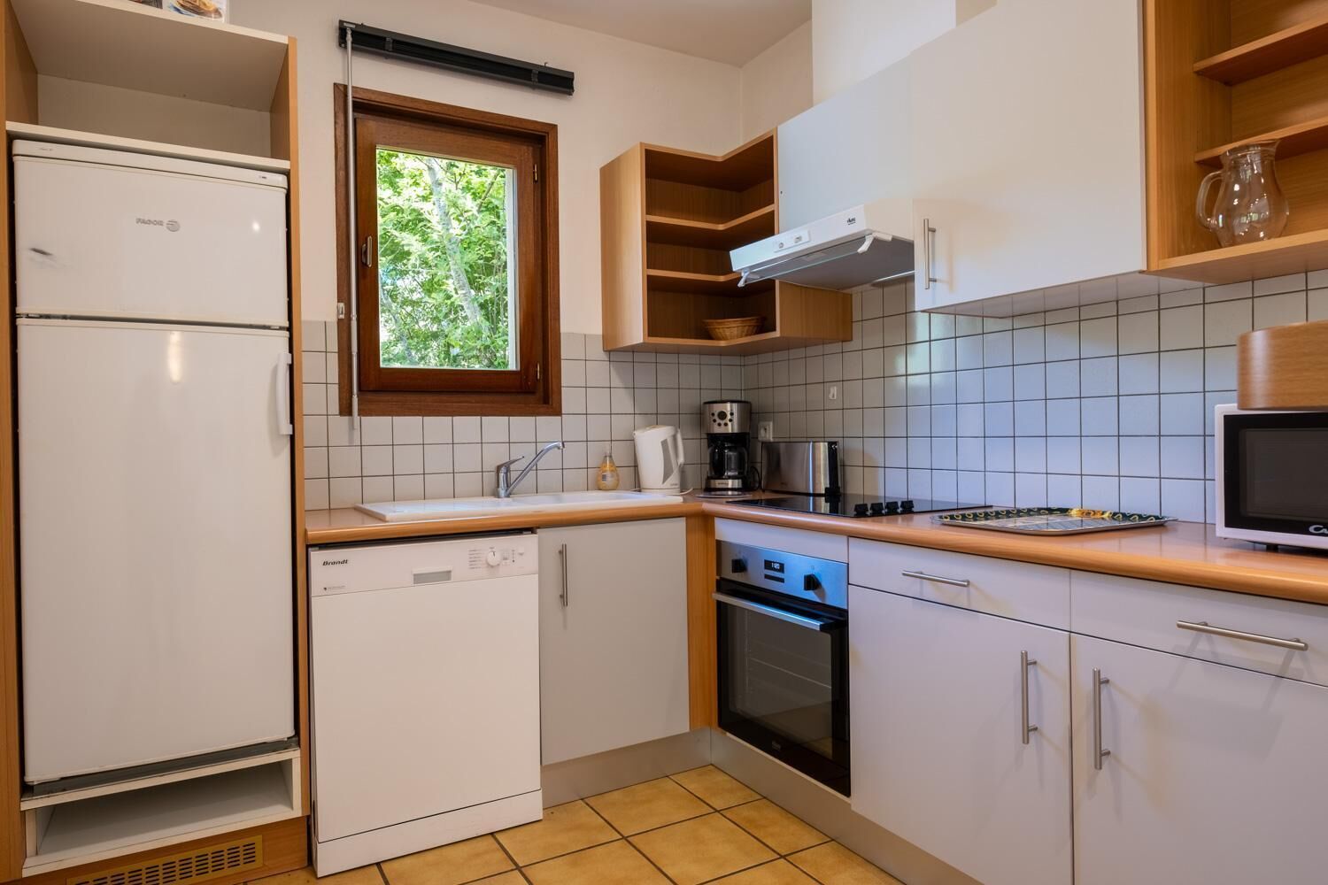 Una cocina compacta con electrodomésticos blancos, una ventana y estantes de madera.