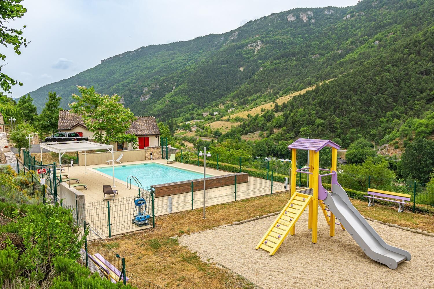 Un parque infantil con un tobogán y una zona de piscina, rodeado de colinas y vegetación.