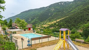A playground with a slide and a pool area, surrounded by hills and greenery. - Gîte 4/6 pers. Premium Plus at Castel de la Peyre (LES VIGNES)