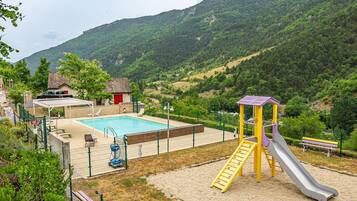 Un parque infantil con un tobogán y una zona de piscina, rodeado de colinas y vegetación.