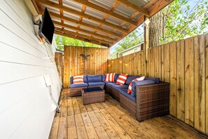 Un espacio de estar al aire libre techado con piso de madera, un sofá modular con cojines y una mesita.