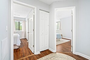 A hallway with a wooden floor, white walls, and a door leading to a bedroom with a bed and a window. - Chic Downtown Auburn Townhome! 2/1.5 (Auburn)