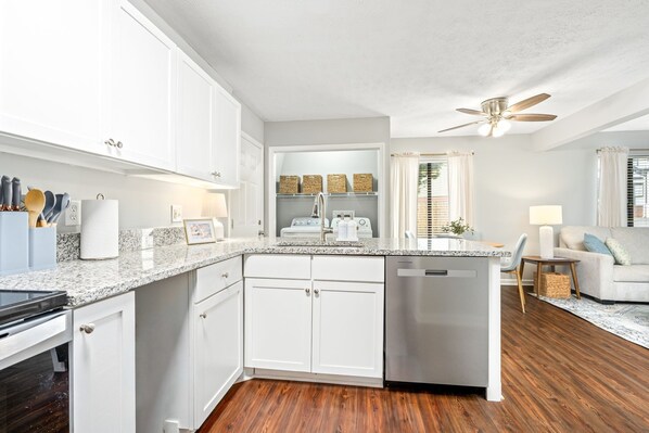 A modern kitchen with white cabinetry, a granite countertop, a built-in dishwasher, and a ceiling fan. - Chic Downtown Auburn Townhome! 2/1.5 (Auburn)