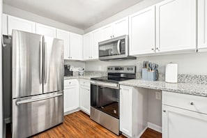 A modern kitchen with stainless steel appliances, white cabinetry, and a granite countertop. - Chic Downtown Auburn Townhome! 2/1.5 (Auburn)