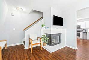 A modern living room with a fireplace, wooden flooring, a TV mounted on the wall, and a staircase leading to another level. - Chic Downtown Auburn Townhome! 2/1.5 (Auburn)