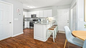A modern kitchen with white cabinets, a central island with bar stools, and a dining area with a table and chairs. - Chic Downtown Auburn Townhome! 2/1.5 (Auburn)