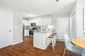 Una cocina moderna con armarios blancos, una isla central con taburetes y un área de comedor con mesa y sillas.