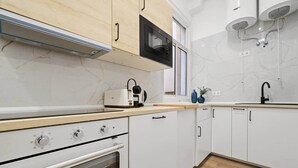 A modern kitchen with white cabinets, a built-in oven, a microwave, and a window above the sink. - Classic Malasaña (Madrid)