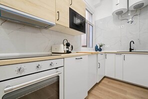 A modern kitchen with white cabinets, a built-in oven, a microwave, and a window above the sink. - Classic Malasaña (Madrid)