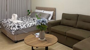 Et moderne hotelværelse med en seng, en sofa, et rundt træbord og et billede på væggen.