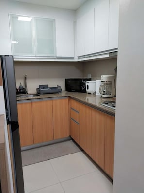 A kitchen with white cabinets, a black microwave, a coffee maker, and a refrigerator. - Klassi Executive Comfort Near NAIA | Fast WiFi & Safe Stay (Pasay City)