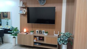 En moderne stue med et fladskærms-tv monteret på en trævæg, et ur og et indbygget tv-møbel med planter og pynteting.