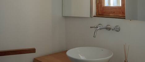A bathroom with a white sink, wooden countertop, and a mirror above it.