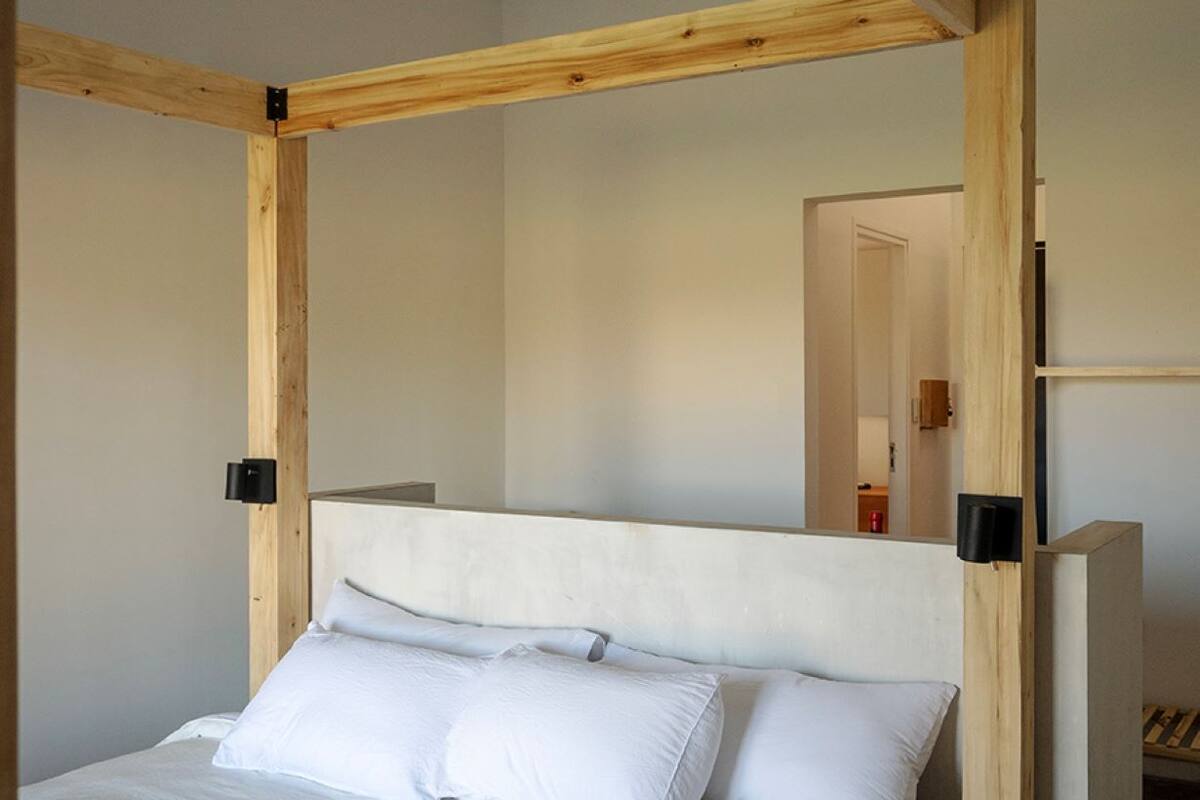 Un dormitorio con una cama de madera con dosel, ropa de cama blanca y una puerta visible al fondo.