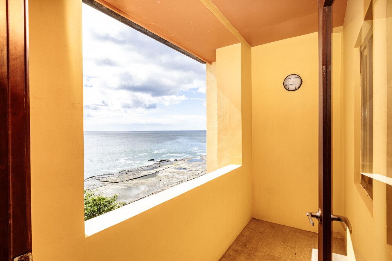 Un petit balcon fermé offrant une vue sur la mer et le rivage rocheux.
