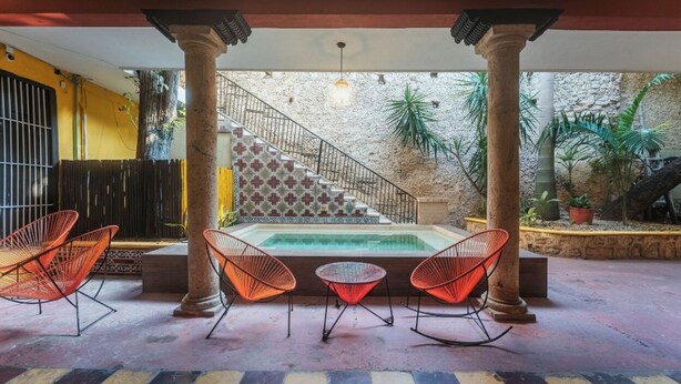 A covered patio with a pool, red chairs, and a staircase leading to an upper level. - Comfortable Room Perfect for Exploring Mérida’s Historic Sights & Culture (Mérida)