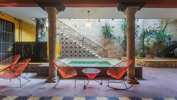 A covered patio with a pool, red chairs, and a staircase leading to an upper level. - 2 Bright Rooms in the Heart of the City, Perfect for Families or Friends (Mérida)