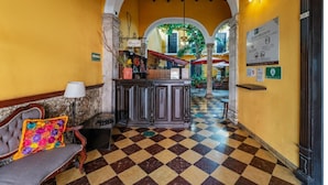 A lobby with a checkered floor, a reception desk, a bench with a colorful cushion, and an arched doorway leading to another area. - 2 Bright Rooms in the Heart of the City, Perfect for Families or Friends (Mérida)