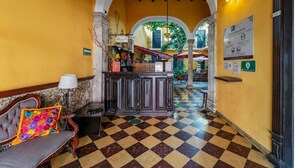 A lobby with a checkered floor, a reception desk, a bench with a colorful cushion, and an arched doorway leading to another area. - Spacious 3 Room Units Perfect for City Adventures and Group Getaways (Mérida)