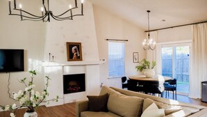 Una sala de estar con chimenea, un sofá, una mesa de comedor con sillas y un televisor montado en la pared.