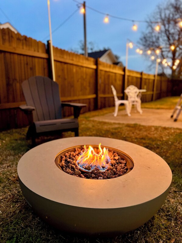 A circular outdoor fire pit with a metal rim and a central fire.