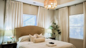 Una cama bien hecha con ropa de cama a rayas, un cabecero y almohadas. Hay dos mesitas de noche con lámparas y un florero con una flor.