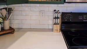 Cocina con armarios verdes, encimera blanca y horno de acero inoxidable.