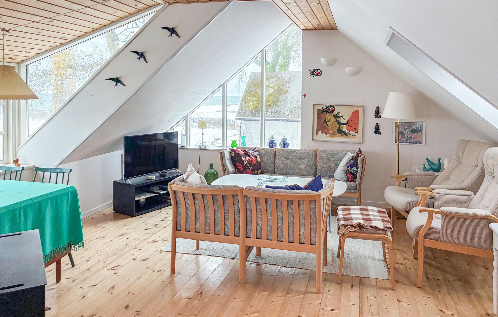 Un acogedor dormitorio en el ático con suelo de madera, televisor, mesa de comedor y sofá.
