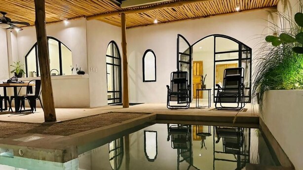 Zona de piscina interior moderna amb parets de vidre transparent, gandules negres i sostre de fusta.
