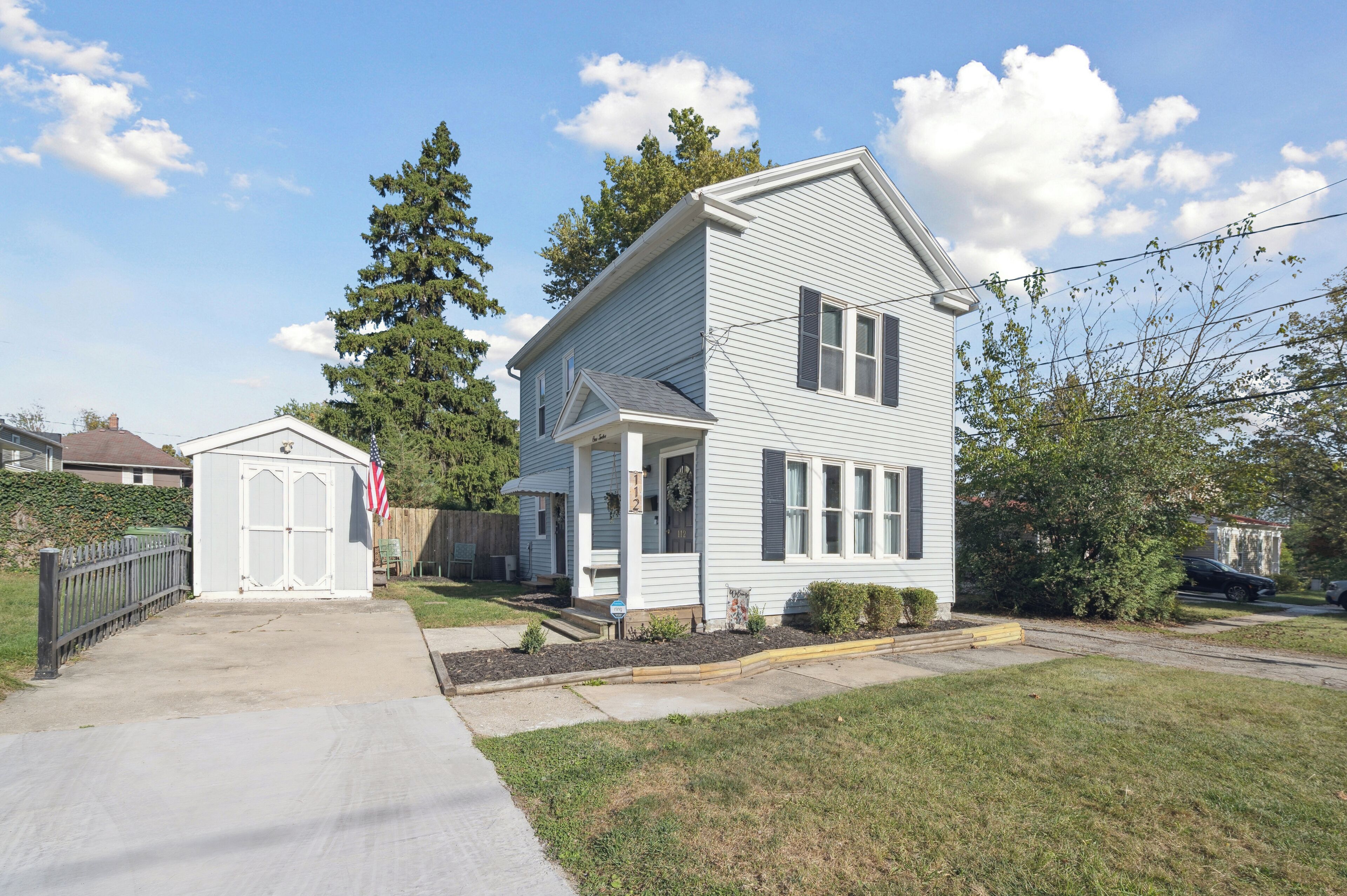A two-story house with a front porch, a garage, and a small shed.