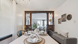 Ein Essbereich mit einem langen Tisch, gedeckt für vier Personen, einem grauen Sofa und einer Deckenleuchte.