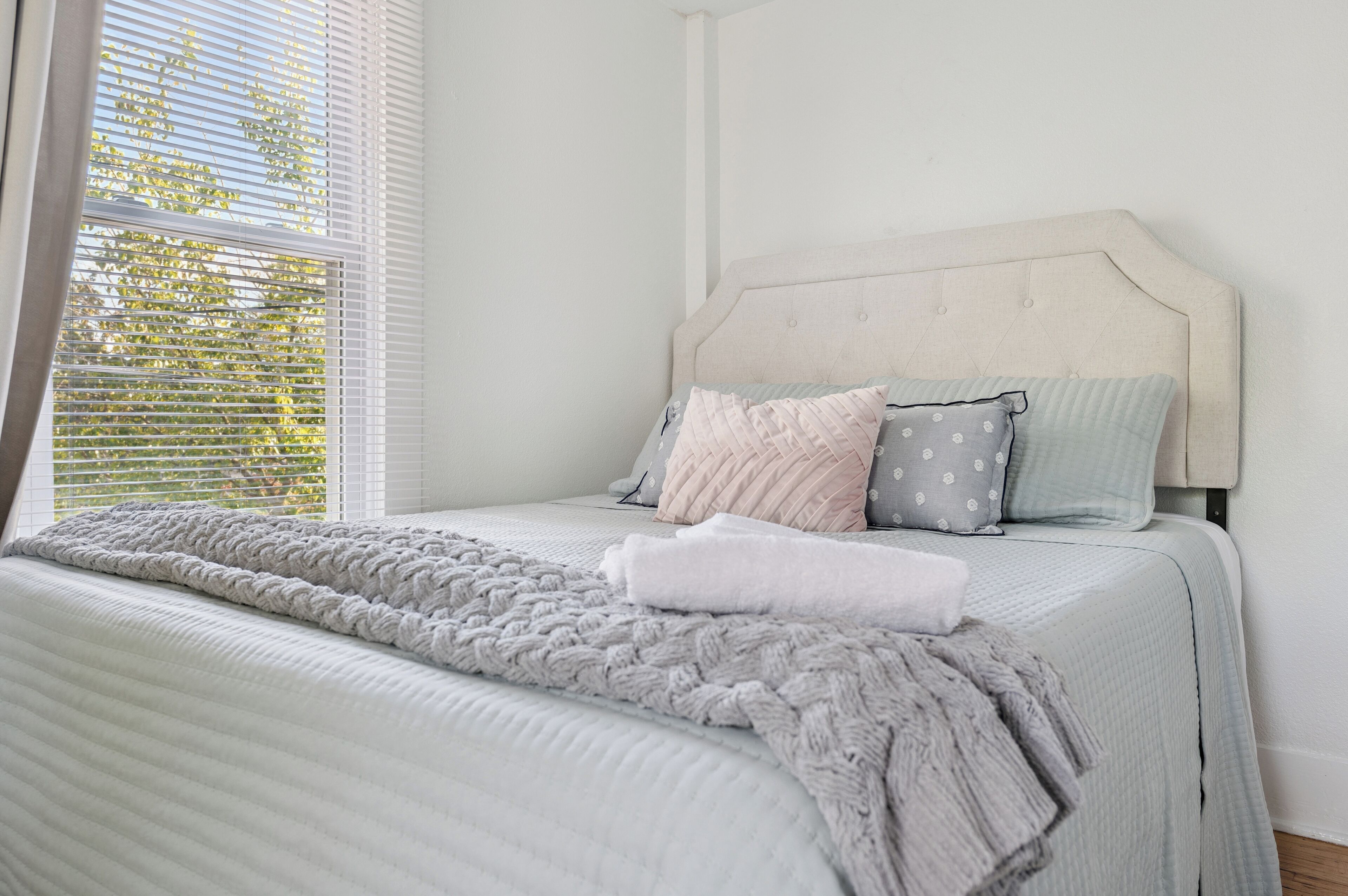 Una cama bien hecha con una manta gris de punto, una almohada blanca y una almohada gris con estampado de lunares.