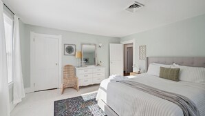 Ein Schlafzimmer mit Bett, Kommode, Stuhl und einem gemusterten Teppich.